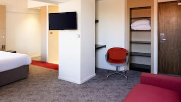 Et hotelværelse med en seng, et fjernsyn ophængt på væggen, en rød stol, et garderobeskab og en rød sofa.