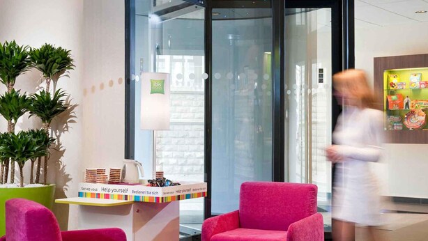 Un espace d’accueil doté d’une porte vitrée, d’un comptoir de réception et de deux fauteuils roses.
