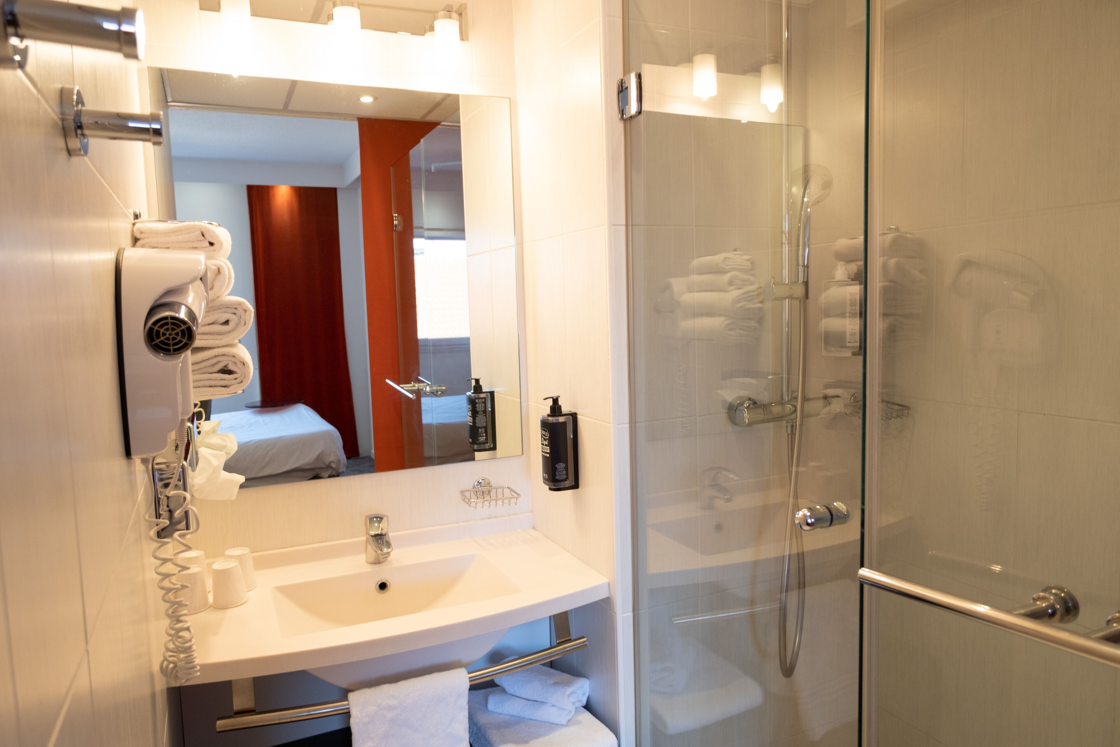 A modern bathroom with a glass-enclosed shower, a white sink with a mirror above, and neatly folded towels on the counter.