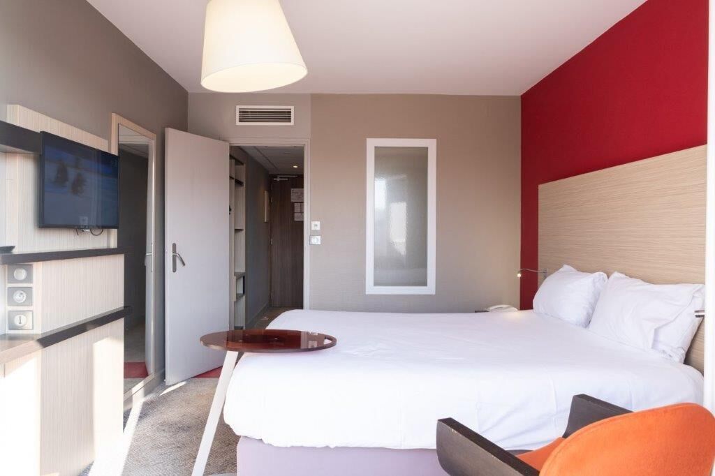 Una habitación de hotel moderna con una cama grande, un escritorio con silla, televisión y una pared de acento roja.