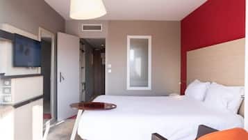 Una habitación de hotel moderna con una cama grande, un escritorio con silla, televisión y una pared de acento roja.