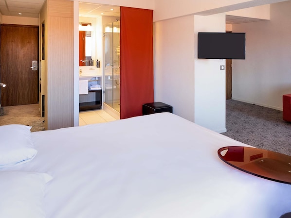 A hotel room with a bed, a TV, a shower, and a bathroom.