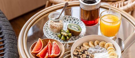 A breakfast tray with a bowl of cereal, sliced bananas, a glass of orange juice, a glass of red juice, a jar of oats, and a bowl of sliced grapefruit.