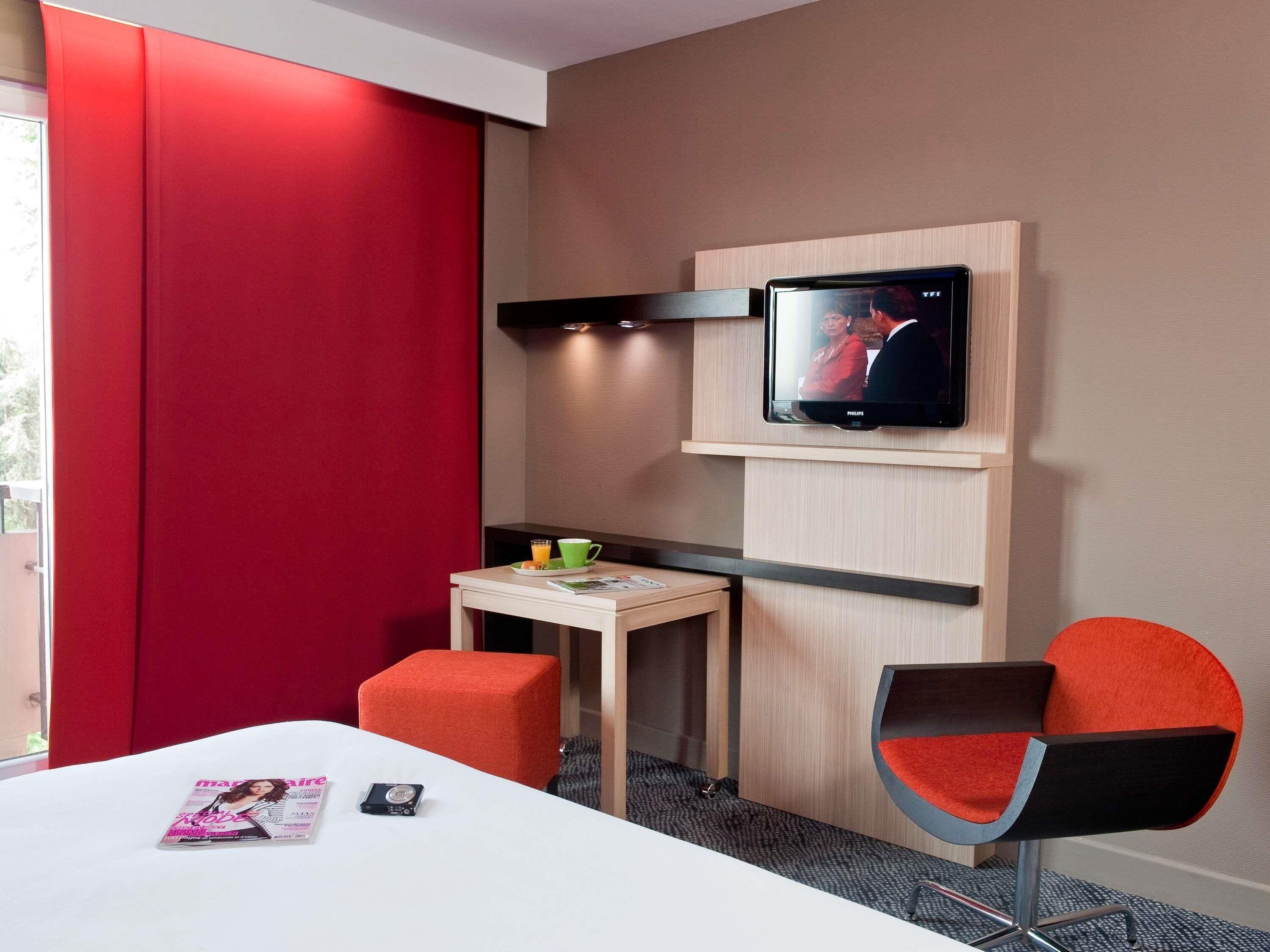 A hotel room with a bed, a desk with a chair, a television, and a magazine on the bed.