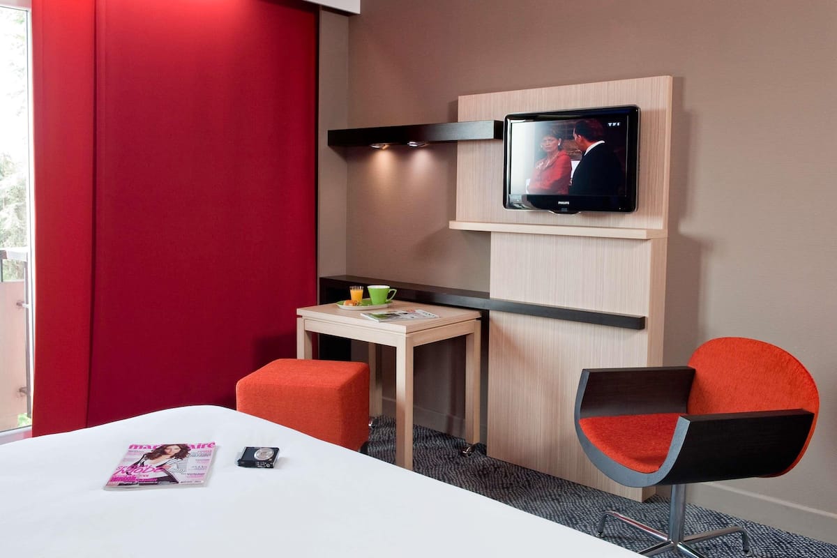 A hotel room with a bed, a desk with a chair, a television, and a magazine on the bed.