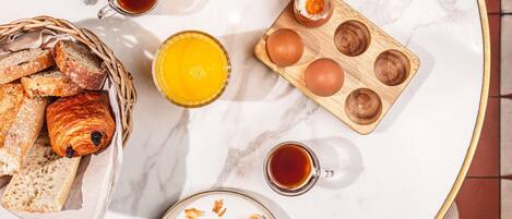 Une table de petit-déjeuner avec du pain, des œufs, du jambon, du fromage et de la confiture.