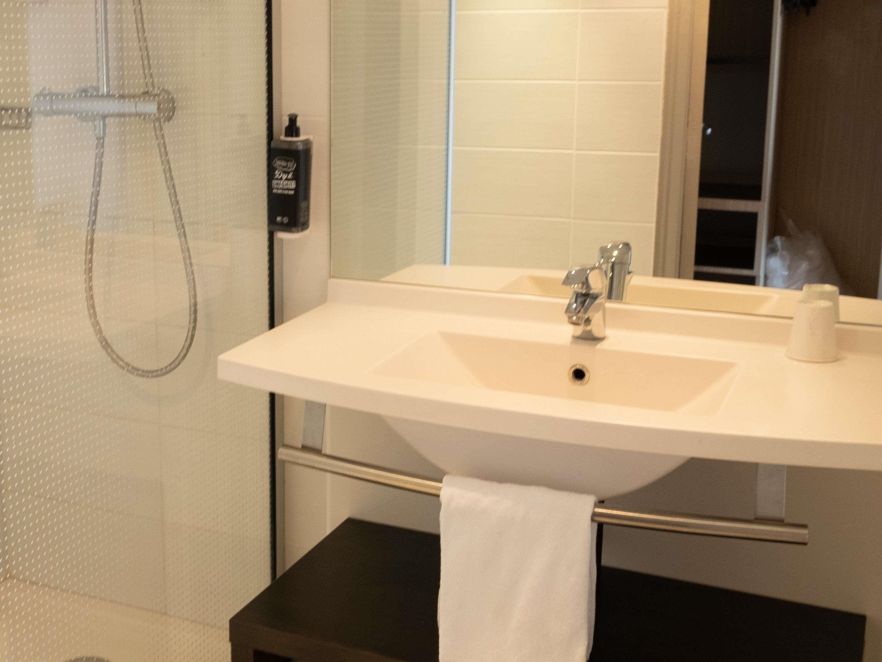 Een badkamer met een witte wastafel, een spiegel en een douche.