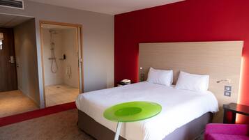 Ein Hotelzimmer mit einem Bett, einem grünen Tisch, einer Dusche und einer roten Wand.
