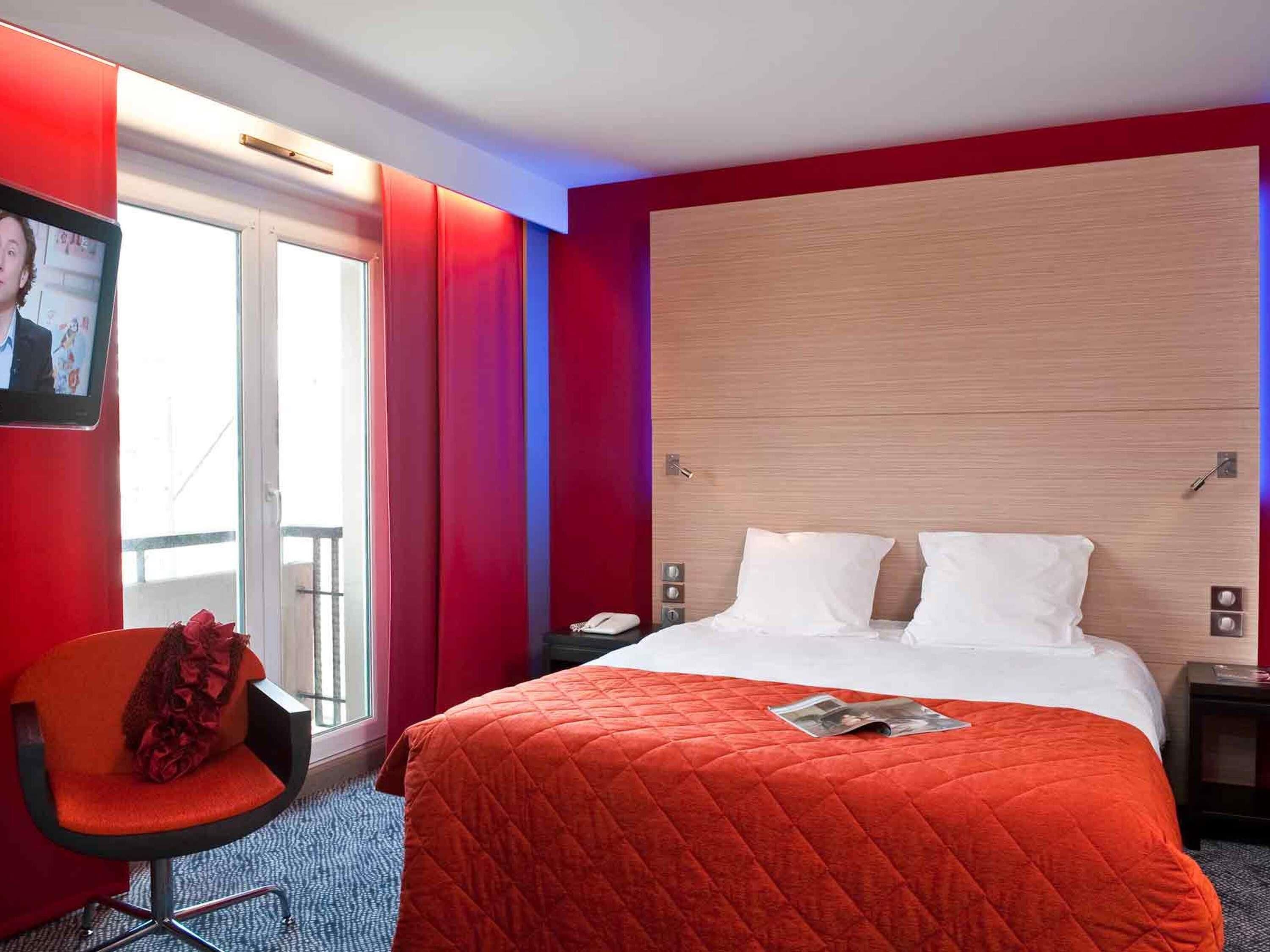 Une chambre d’hôtel avec un lit, une chaise, une table de chevet, un téléviseur fixé au mur et une fenêtre donnant sur un paysage.