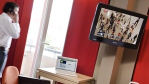 Une chambre d’hôtel avec une télévision diffusant un spectacle de danse, un ordinateur portable sur un bureau, une chaise et une valise.