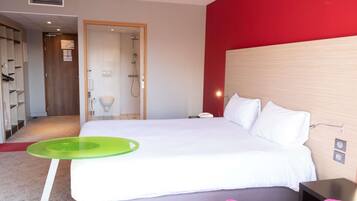 A hotel room with a bed, a green tray, a pink chair, a wooden headboard, and a red accent wall.