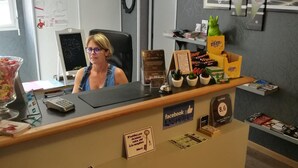 Mostrador de recepción de hotel con computadora, un reloj y un cartel que indica la página de Facebook del hotel.