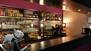 Una zona de bar con estanterías llenas de botellas y vasos, una figurita de perro blanco y un atril para el menú.