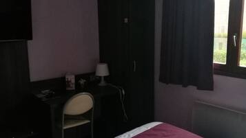 A hotel room with a bed, a desk with a chair, a wardrobe, and a window with curtains.
