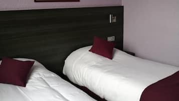 Une chambre d’hôtel avec deux lits simples, chacun agrémenté de draps blancs et d’un oreiller rouge. Un tableau encadré est accroché au mur, au-dessus des lits.