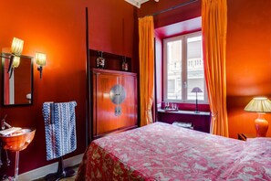 Une chambre d’hôtel avec un lit, une armoire en bois, une fenêtre avec des rideaux, une table de chevet et un miroir.