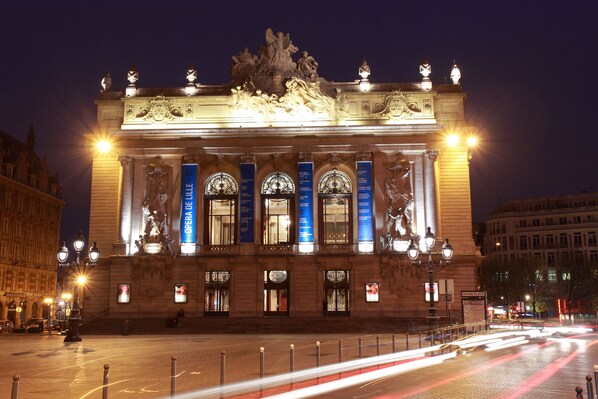 Un edificio imponente de arquitectura clásica, con columnas, estatuas y señalización iluminada.