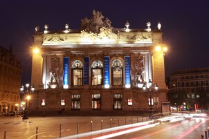 Um edifício imponente com arquitetura clássica, com colunas, estátuas e sinalização iluminada.
