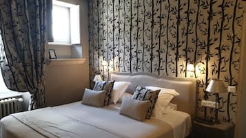 A neatly made bed with white linens and patterned pillows, a bedside table with a lamp, and a wall with a bamboo leaf pattern.
