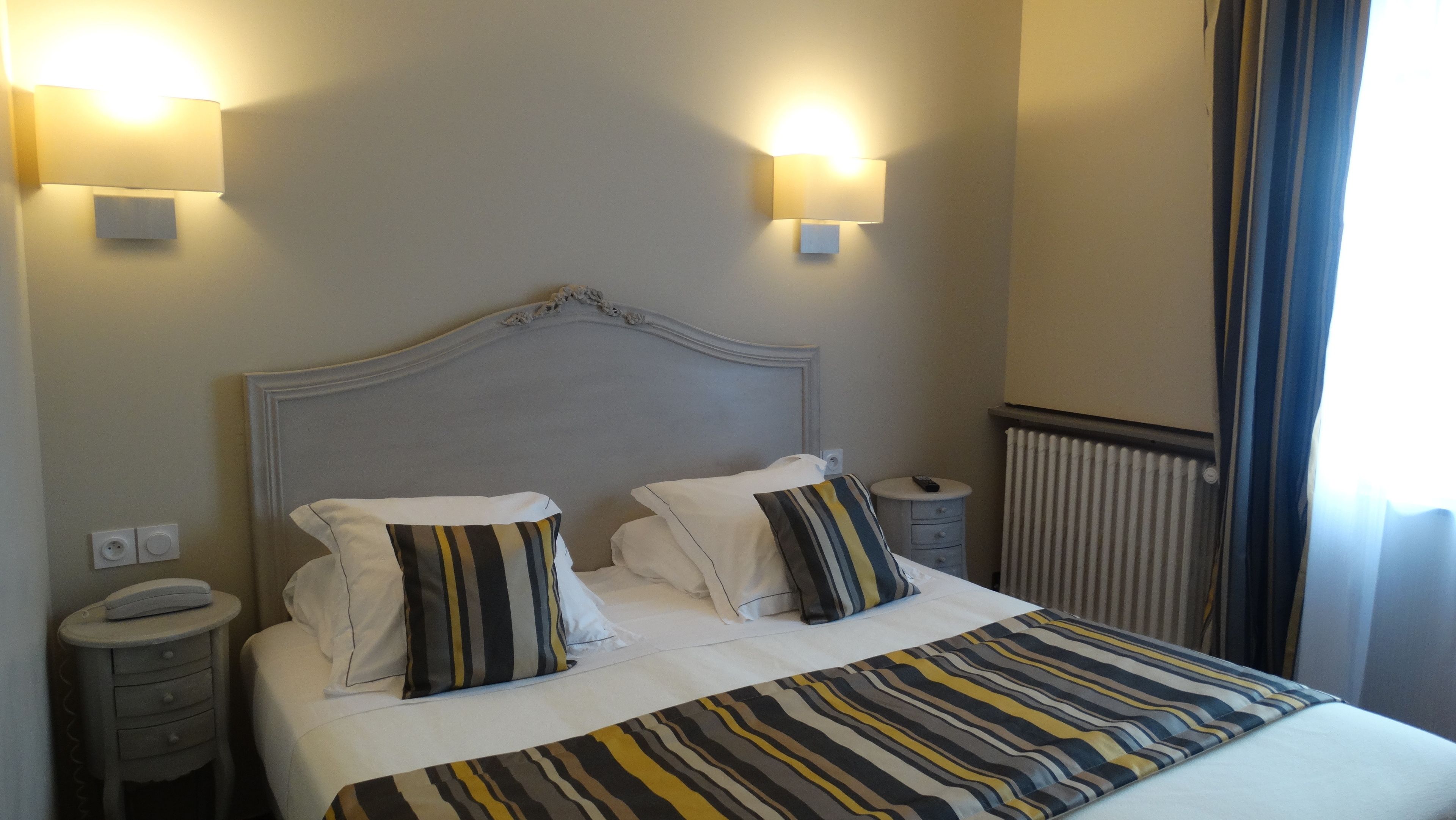 A hotel room with a large bed, two bedside tables, a nightstand, and two wall-mounted lamps.