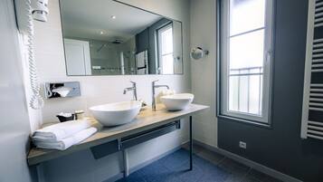 Un baño moderno con dos lavamanos grandes blancos, un espejo amplio y una ventana que proporciona luz natural.