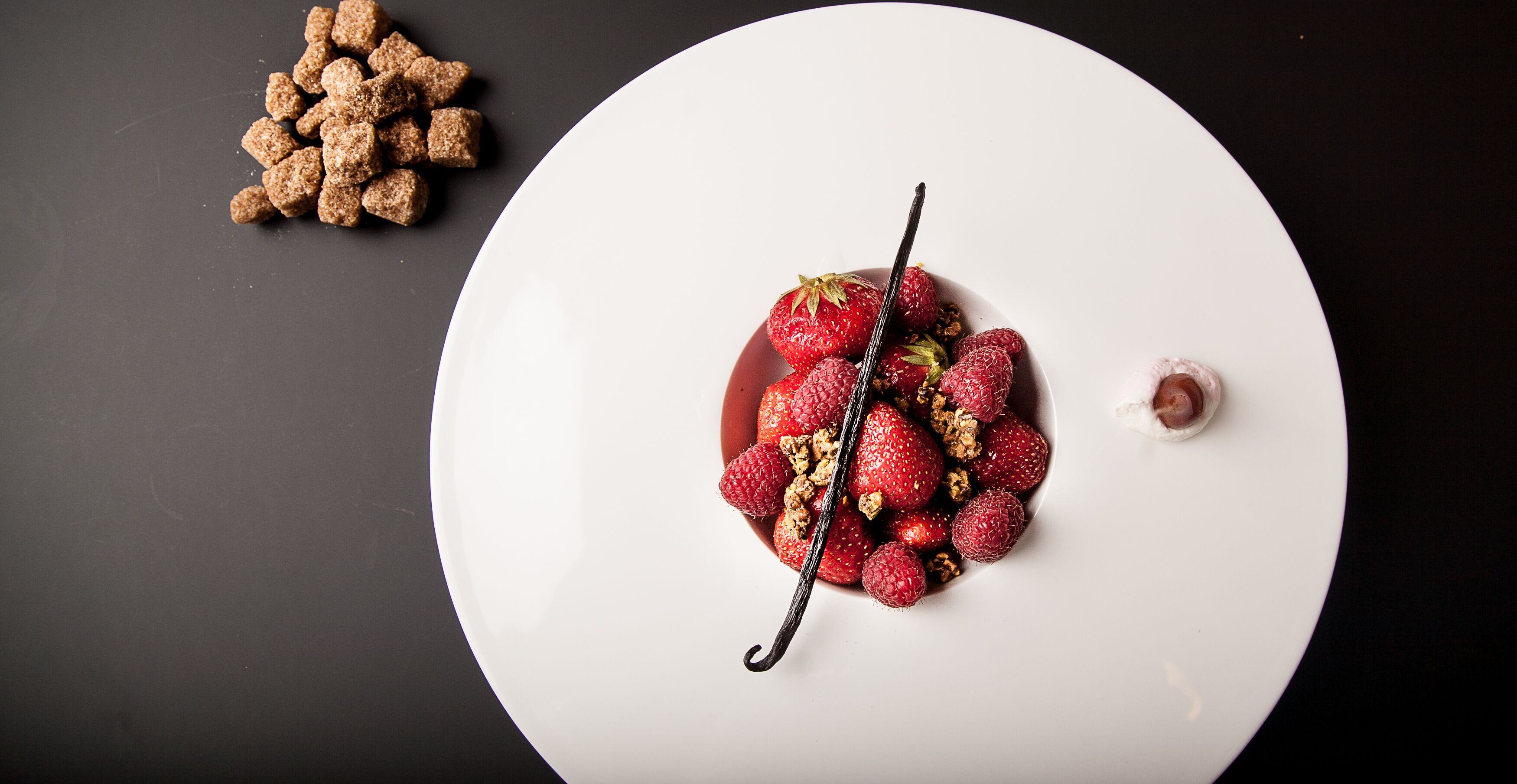 Een wit bord met een dessert van aardbeien en chocoladeschaafsel.
