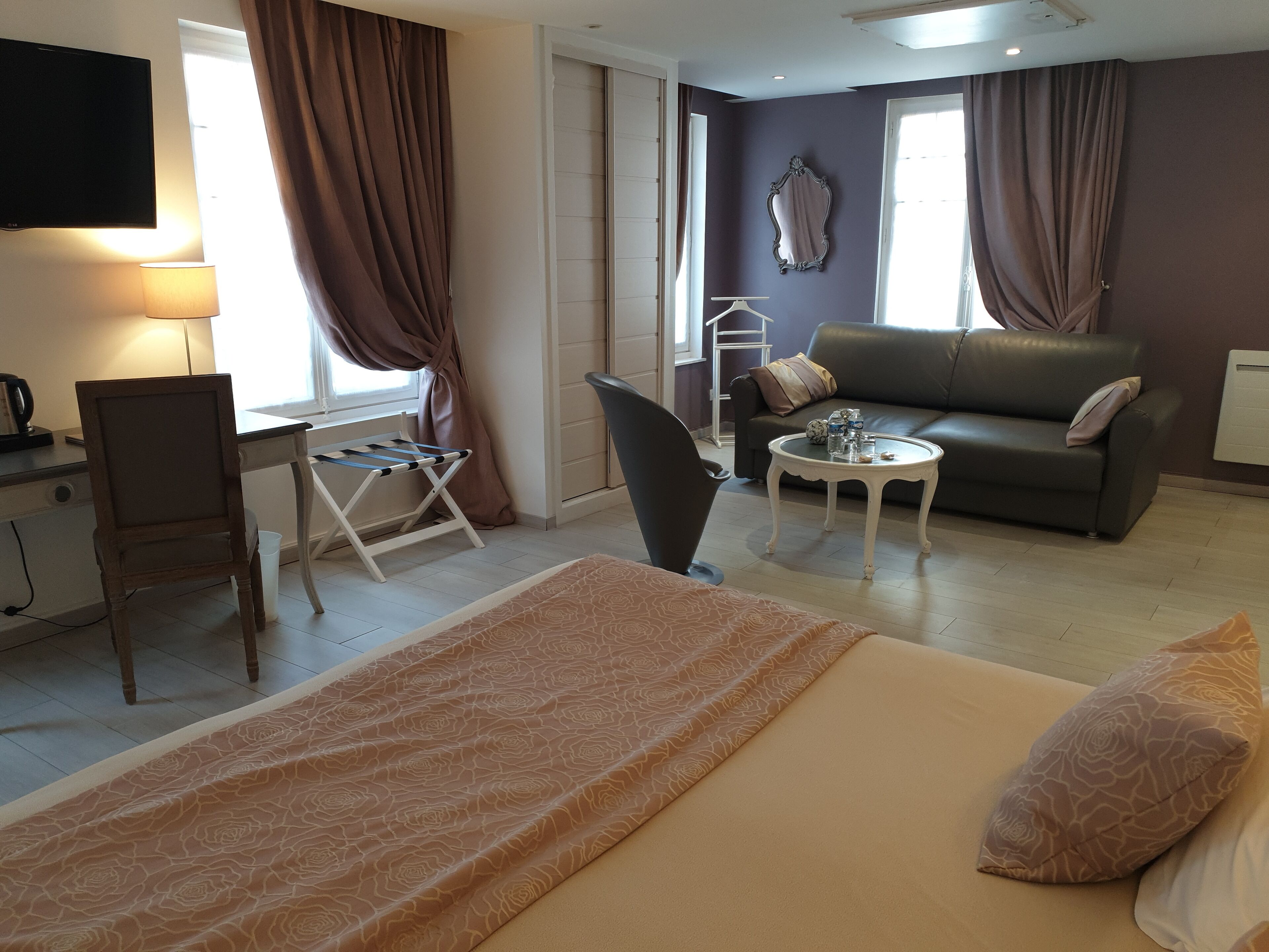 Habitación de hotel con cama, escritorio, silla, sofá, mesita y televisor.