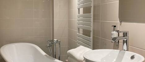 Un baño moderno con una bañera independiente, un tocador con un lavamanos grande y un perchero de toallas en la pared.