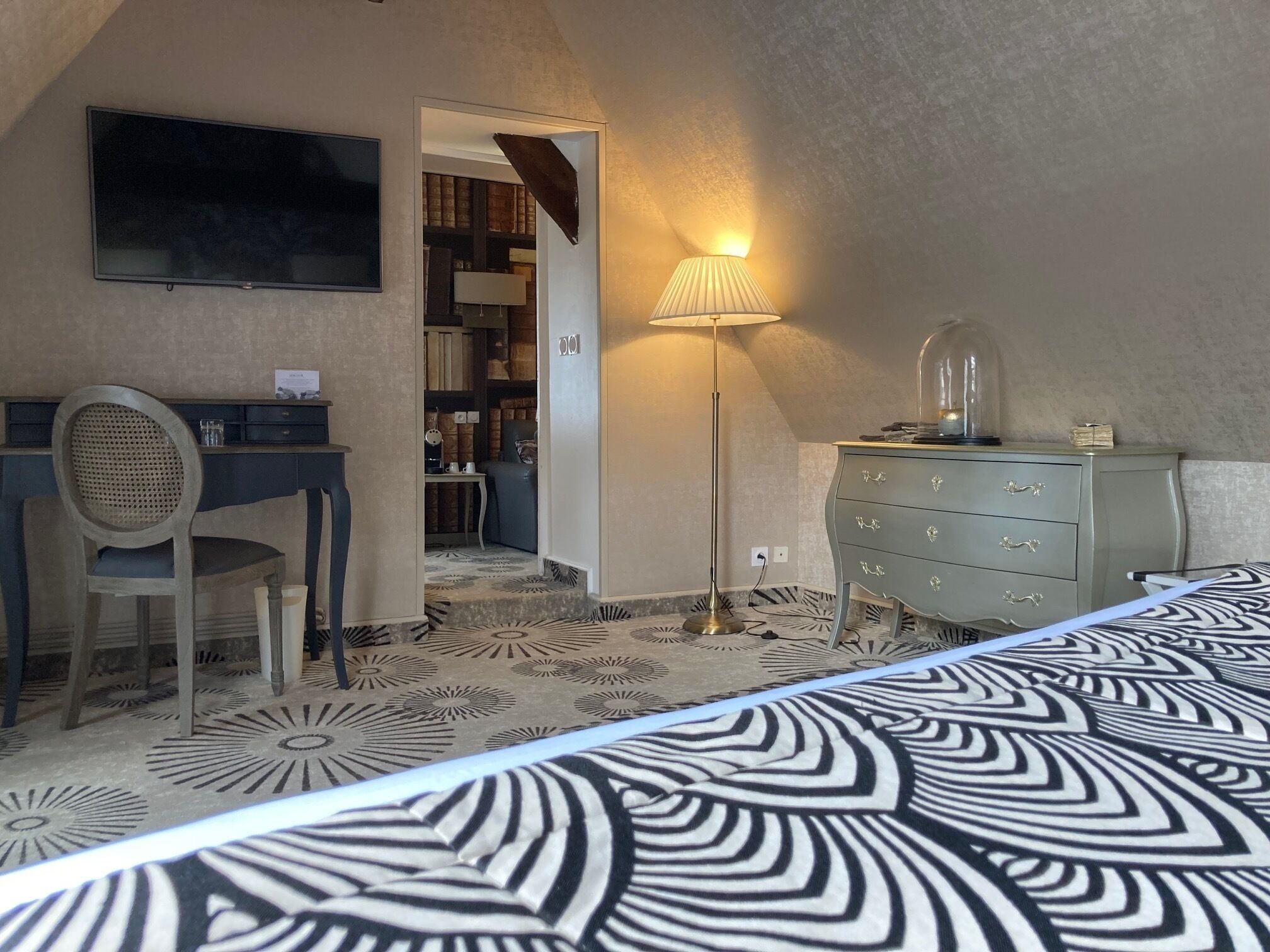Un dormitorio con cama, escritorio, silla, lámpara y cómoda.