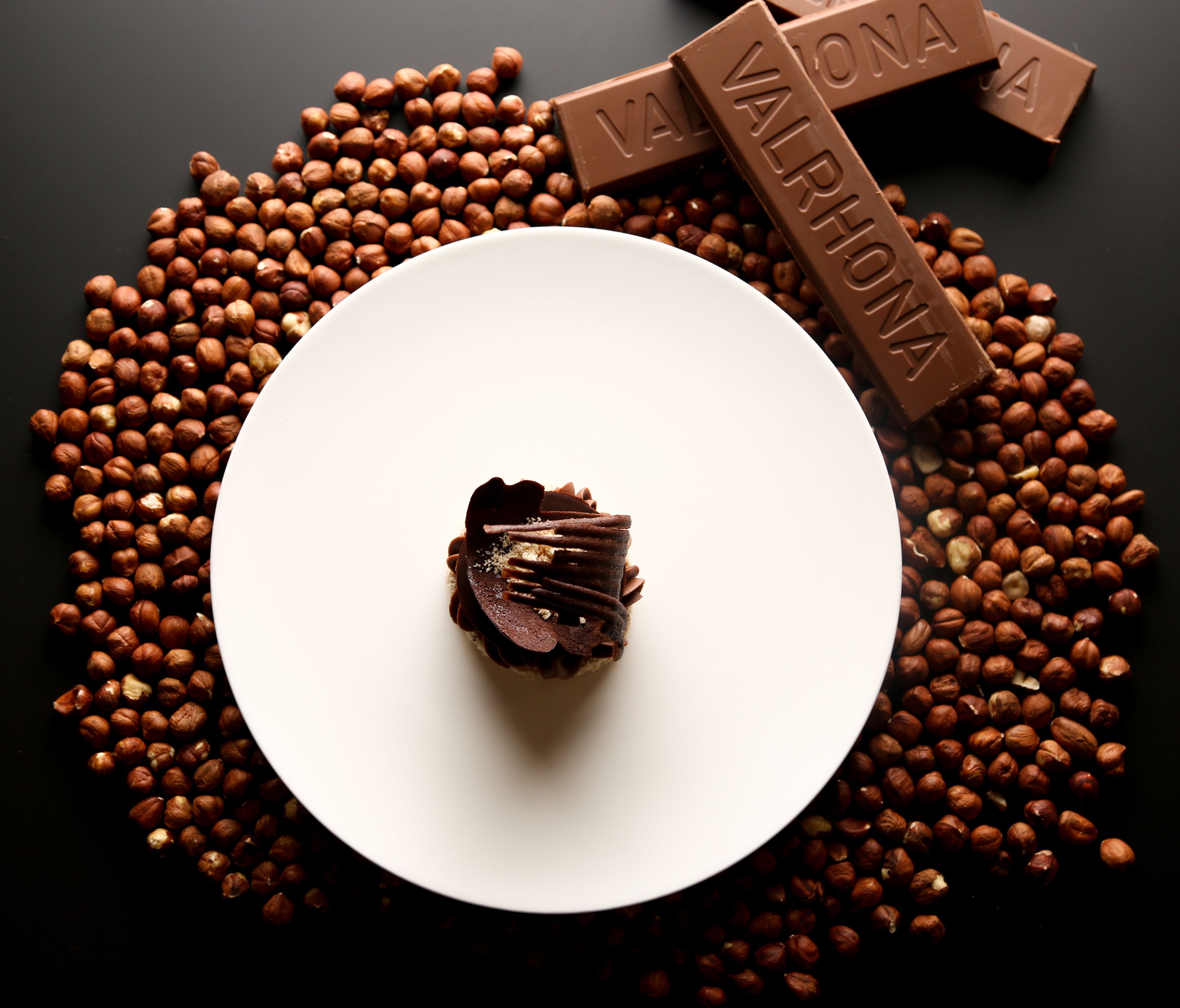 Un postre sobre un plato blanco, rodeado de avellanas y barras de chocolate.