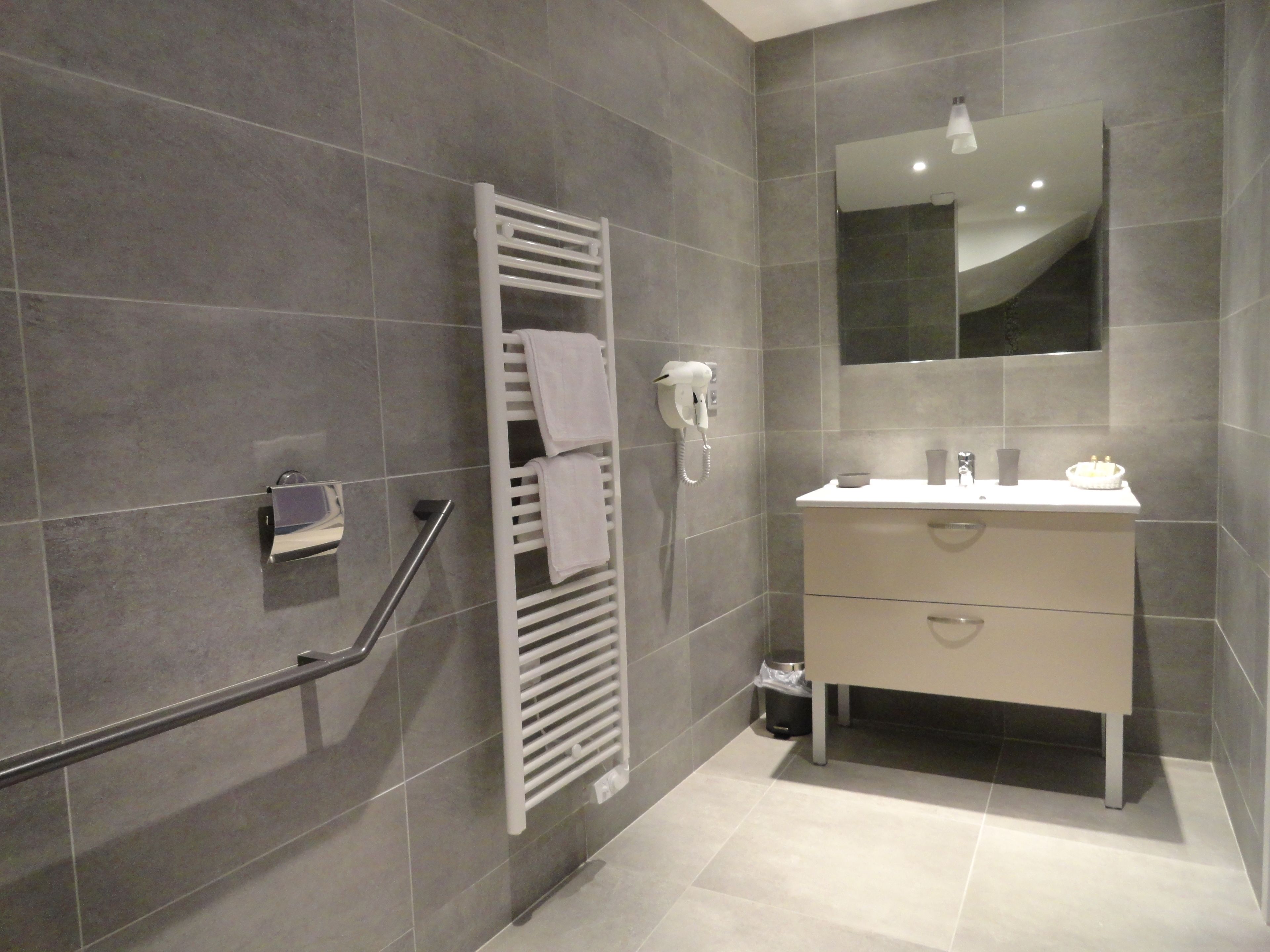 Casa de banho moderna com chuveiro amplo, porta-toalhas, secador de cabelo e toucador com espelho.