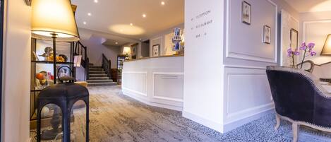 A hotel lobby with a reception desk, a staircase, and a bar area.