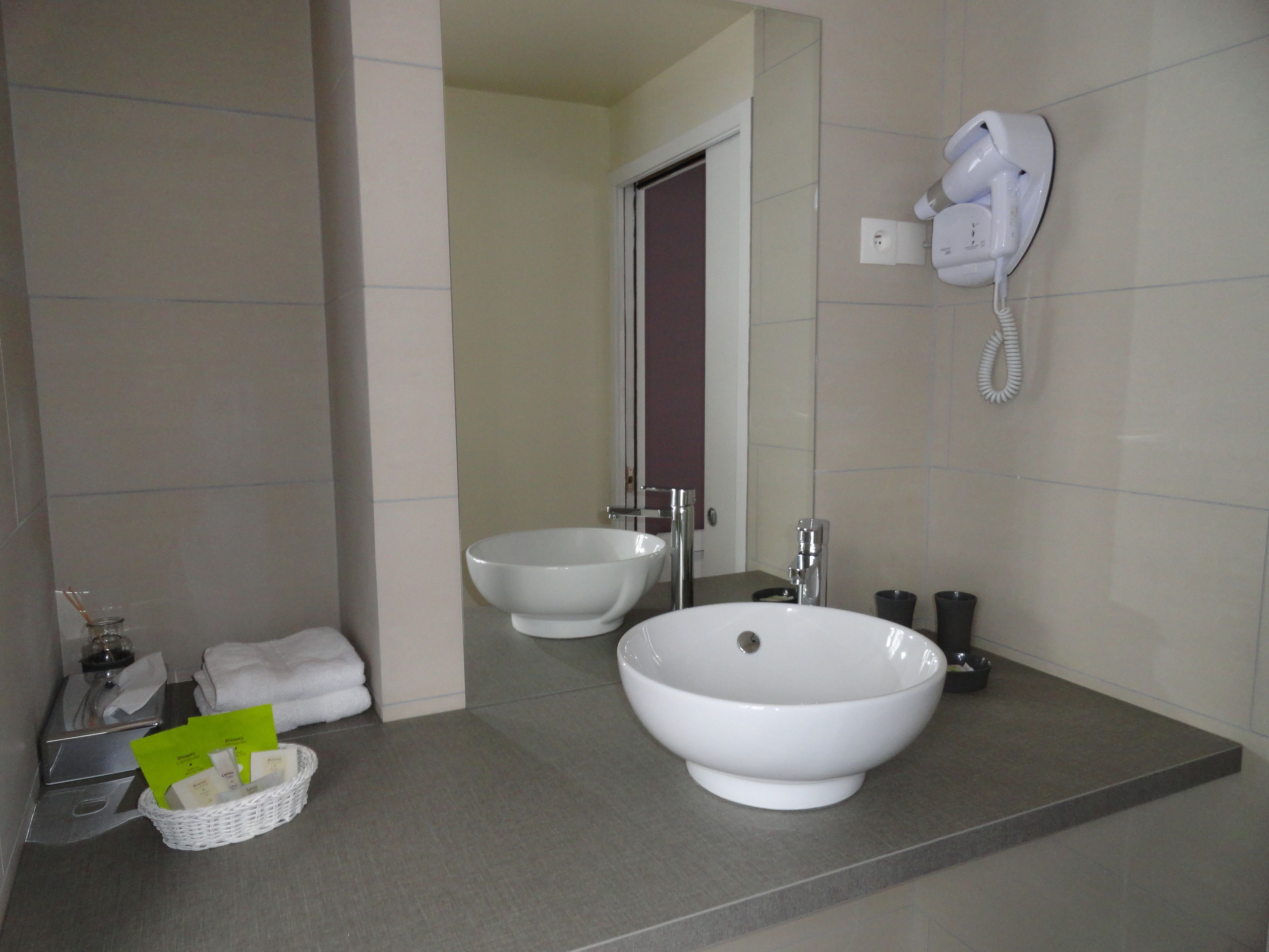 A bathroom with two sinks, a hairdryer mounted on the wall, and a basket with toiletries on the counter.