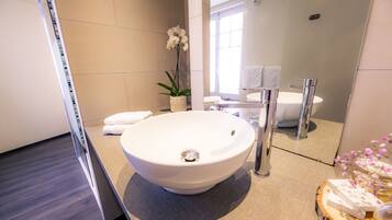 A modern bathroom with a large white sink, a mirror, and a potted orchid.