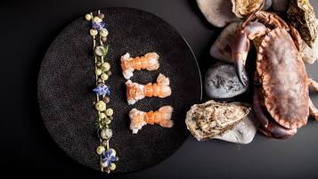 Un piatto nero con una texture particolare, diversi gamberi e una ghirlanda decorativa di perle e fiori.