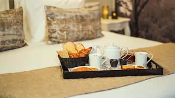 A breakfast tray on a bed with bread, pastries, and coffee cups.