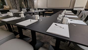 Un salón de conferencias con varias mesas, cada una con cuadernos, bolígrafos y vasos de agua.