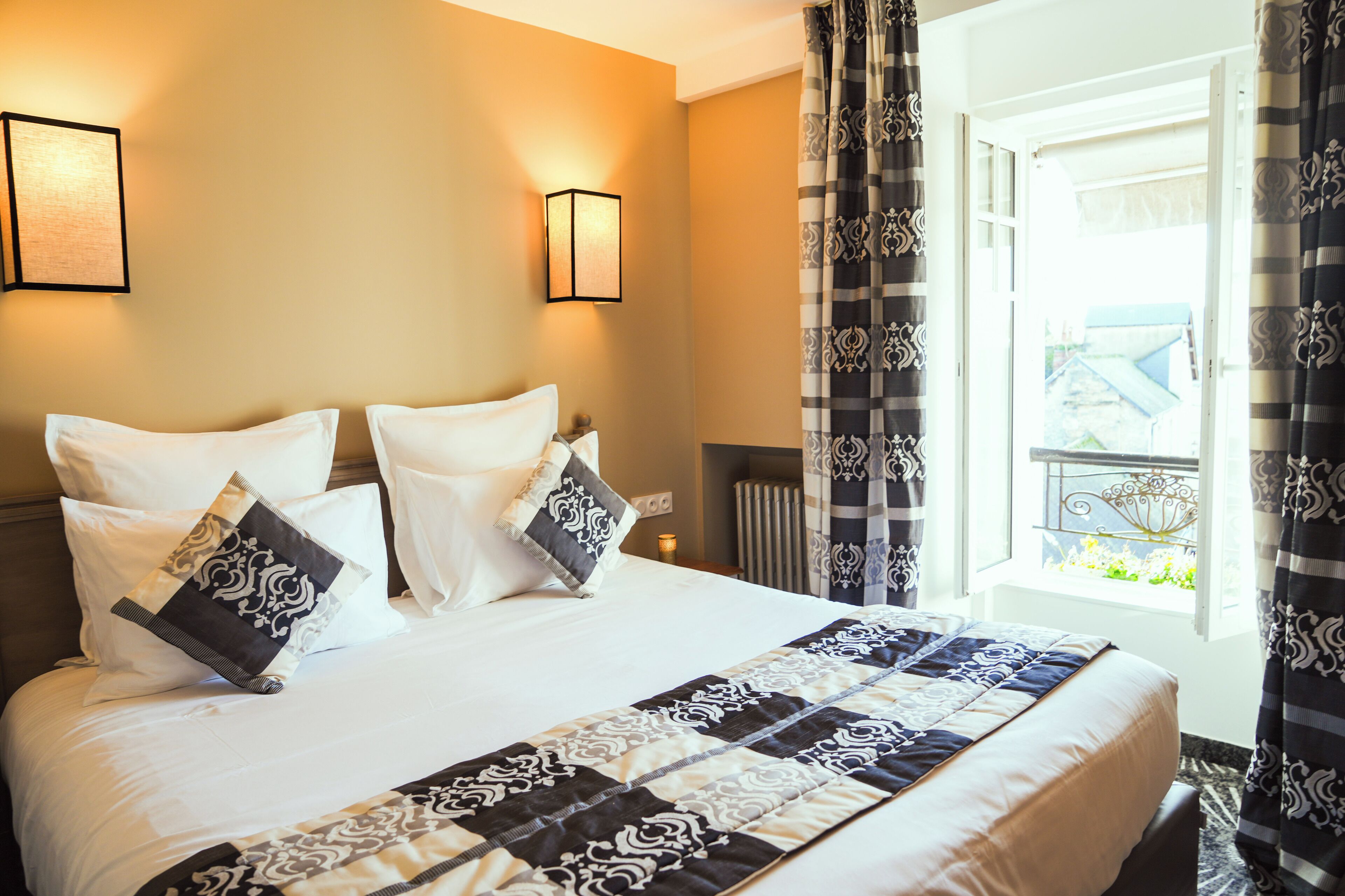 A hotel room with a large bed, two wall-mounted lamps, and a view of the outside through a window with curtains.