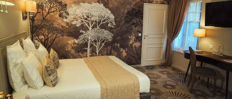 A hotel room with a bed, a desk, a chair, a TV, and a wall mural.