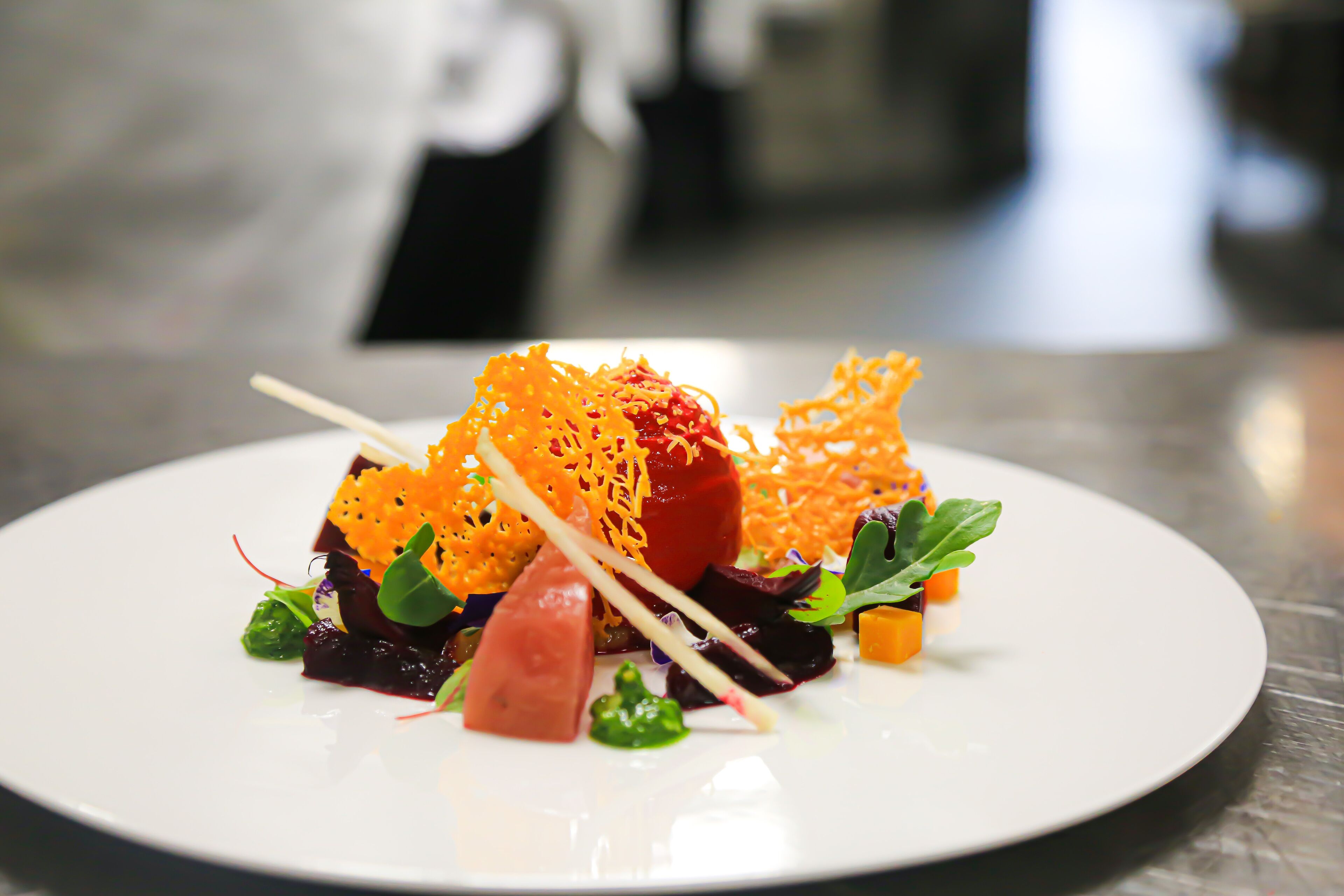A white plate with a variety of food items, including a red fruit, green vegetables, and orange shredded elements, arranged on a table.