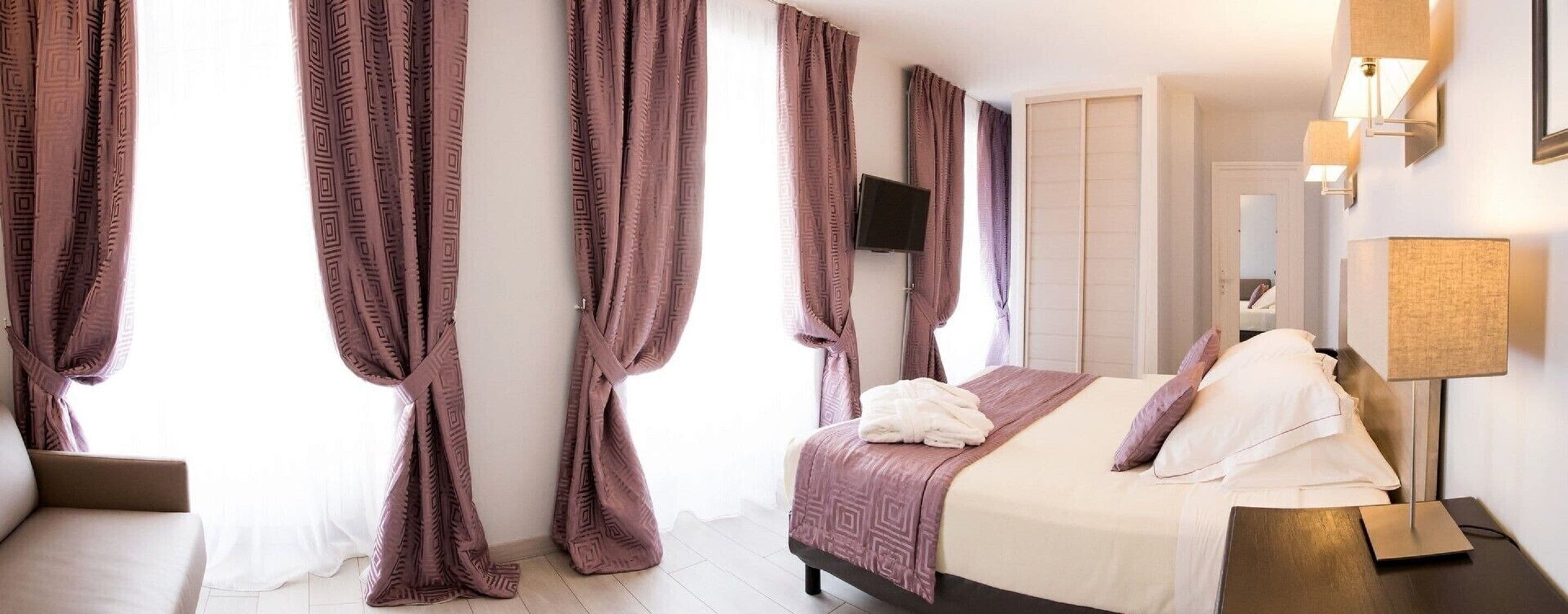 A hotel room with a bed, a TV, a bedside lamp, and curtains.