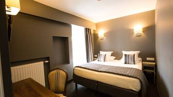 A hotel room with a bed, bedside table, chair, lamp, and wall-mounted light.