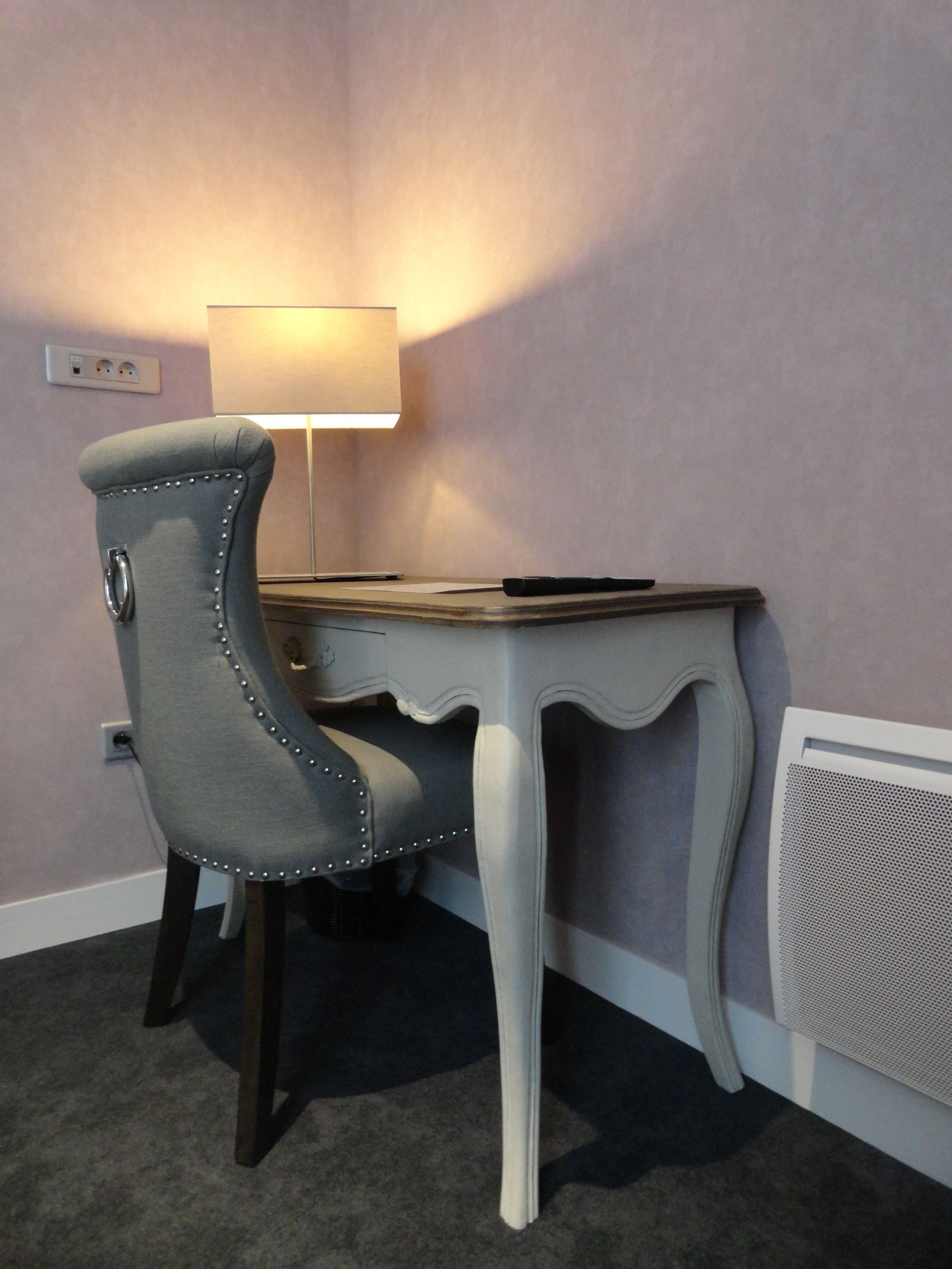 A room with a desk, chair, lamp, and radiator.