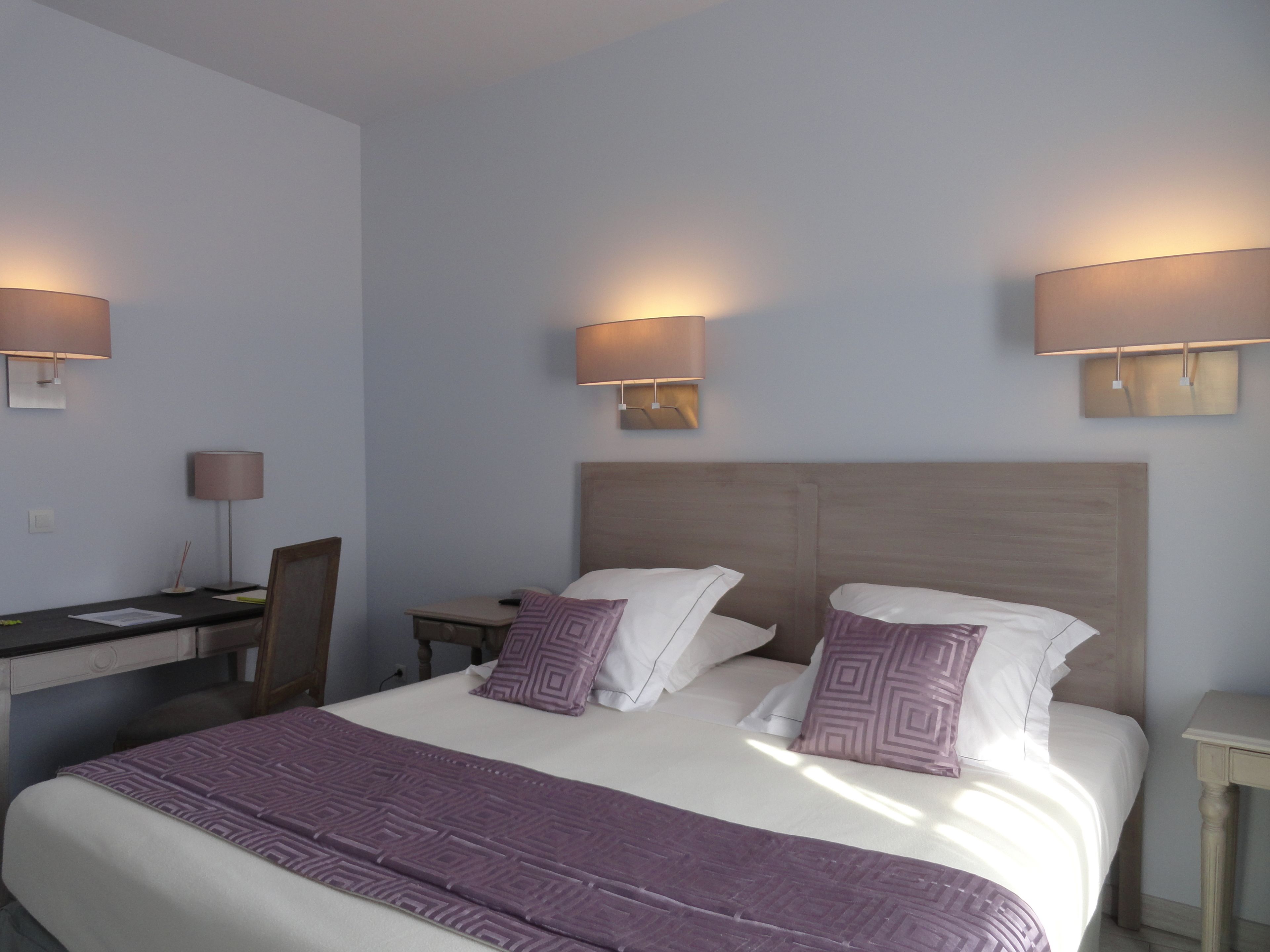 A hotel room with a large bed, two bedside lamps, a desk with a chair, and a small table.