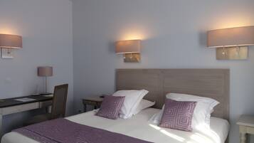 A hotel room with a large bed, two bedside lamps, a desk with a chair, and a small table.
