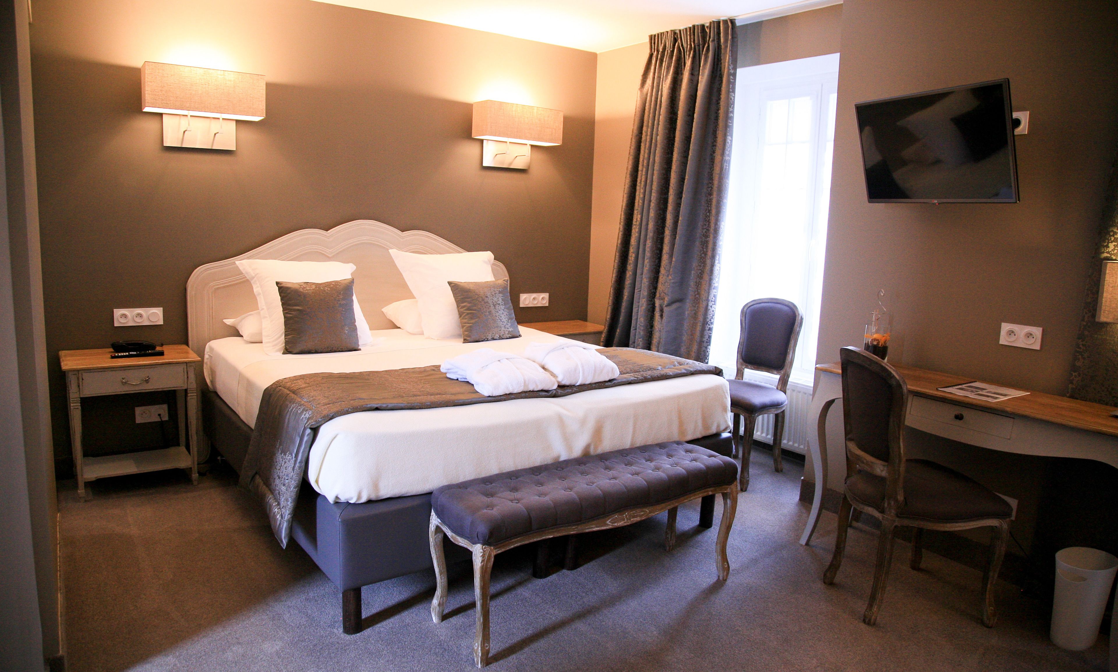 A hotel room with a large bed, bedside tables, a desk, a chair, and a TV on the wall.