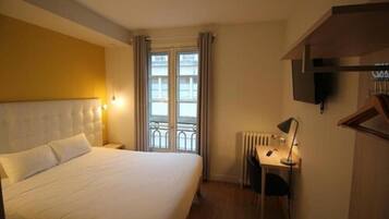 A hotel room with a large bed, a desk with a chair, a radiator, and a television mounted on the wall.