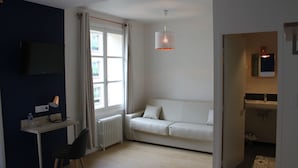 Una habitación de hotel moderna con un sofá blanco, un escritorio con lámpara, televisor y una lámpara colgante.