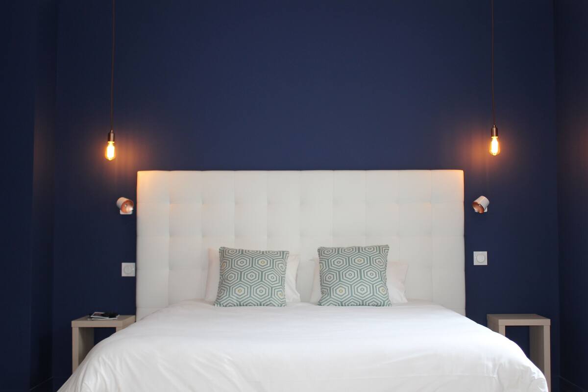 Une chambre à coucher avec un grand lit, deux tables de chevet et une tête de lit ornée d’un motif géométrique.