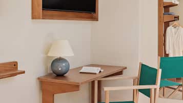 Ein Zimmer mit einem Holztisch, einem Stuhl, einer Lampe, einem Fernseher und einem Kleiderständer.